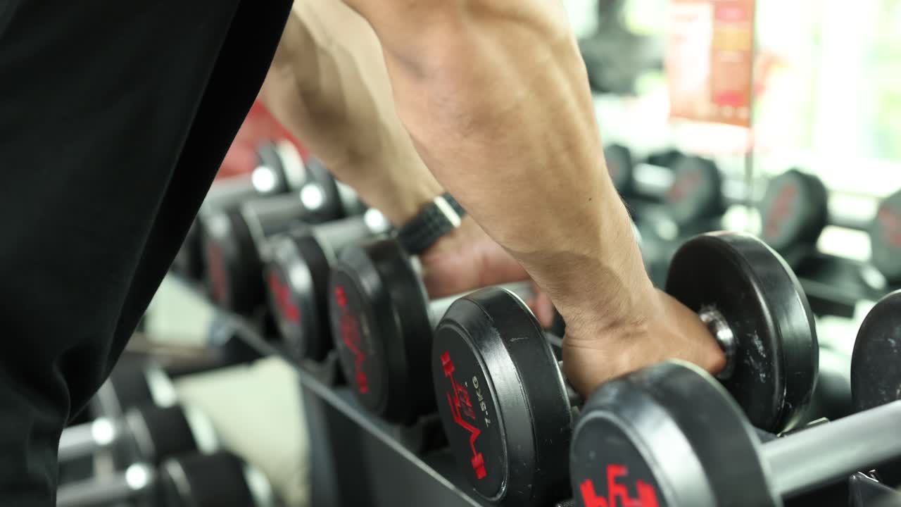 A man in a gym selects dumbbells from a rack. Bright lighting highlights the focused action and modern equipment
