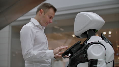 el hombre en el centro comercial se comunica con un asesor robot. tienda moderna y vendedor robot. robot ayuda a un hombre en el centro comercial.