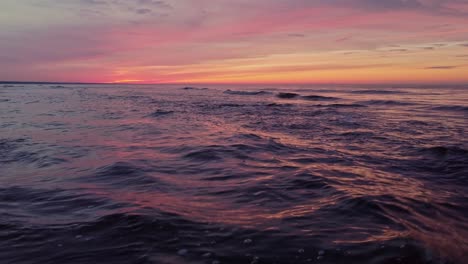 Drone-flying-low-over-shore-of-a-beach-under-a-magical-sunset-in-the-golden-hour