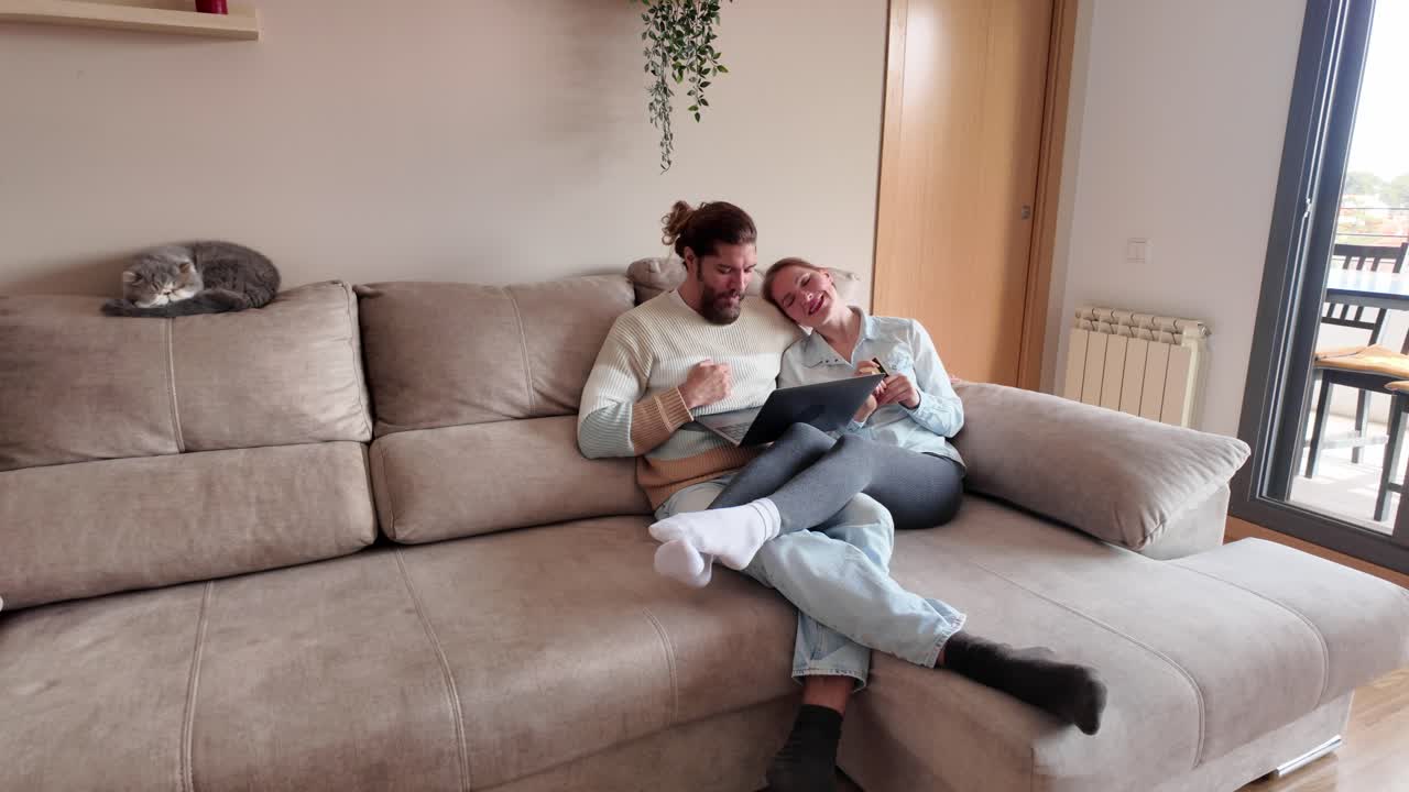 Couple using laptop on sofa with cat
