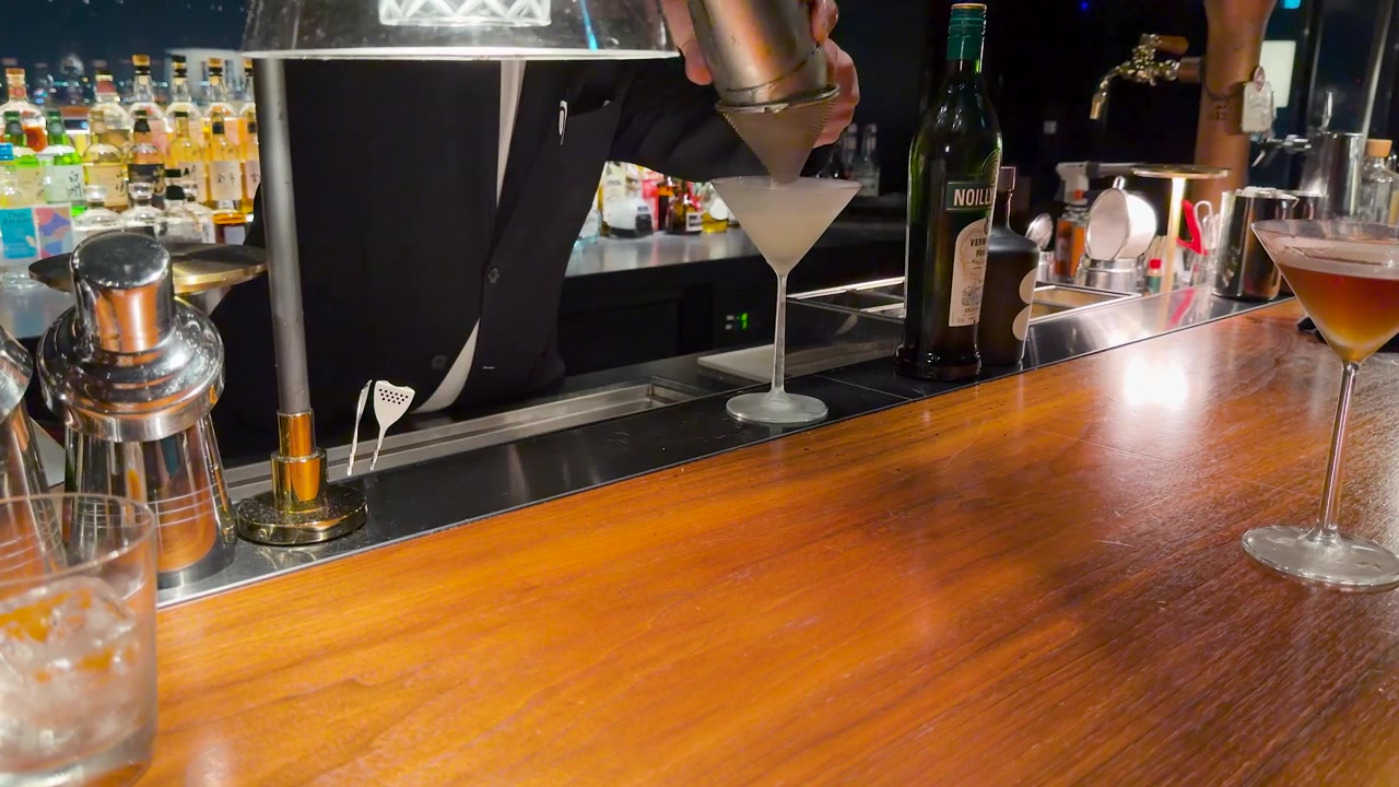 Un barista professionista versa un cocktail ghiacciato in un bicchiere da martini su un bancone di legno
