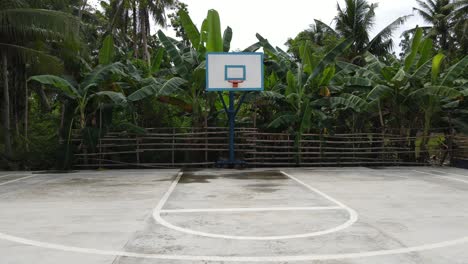 aerial drone fly low above cemented basketball field in tropical jungle surroundings