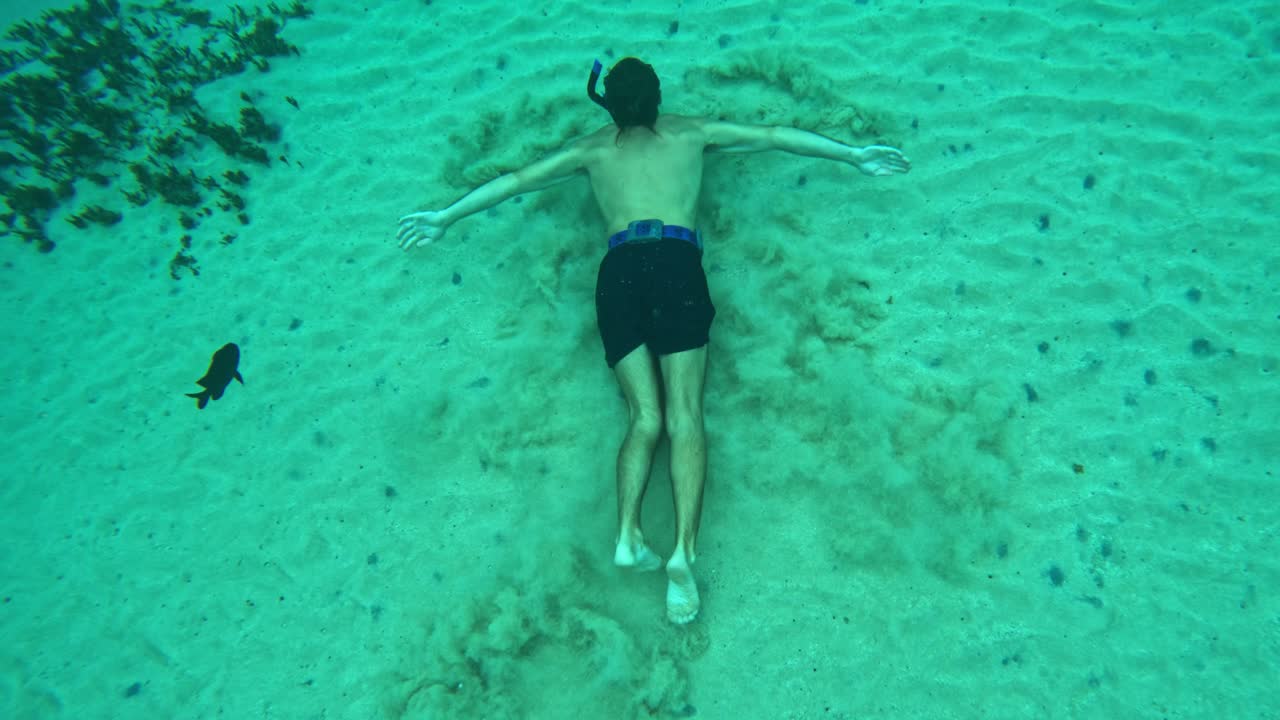Man swims along sandy bottom of deep ocean water as sand floats from his paddling