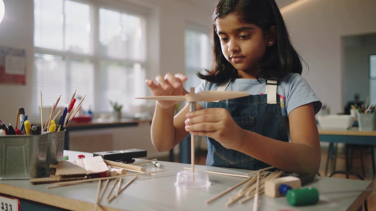 Placing clear base and dowel, girl in overalls centering blade at classroom table, testing balance