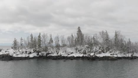 waves crashing on rocky islet with pine trees during winter. - aerial shot