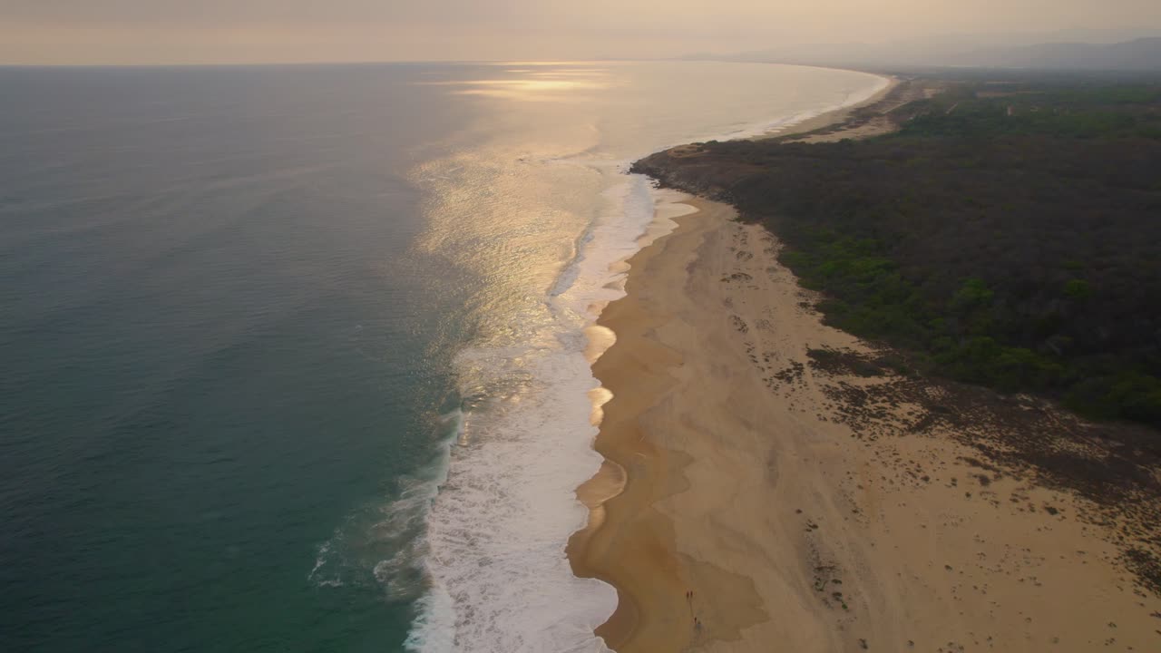 vista aérea volando sobre la dorada playa de oaxaca iluminada por el sol mientras las olas del océano bañan la costa arenosa de méxico