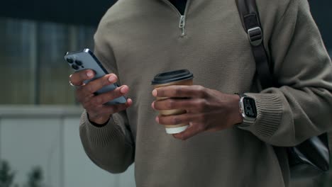 man using smartphone and drinking coffee outdoors