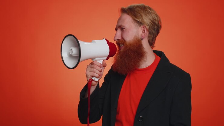 Uomo barbuto sorridente che parla con un megafono, proclamando notizie, annunciando a gran voce una promozione di vendita.