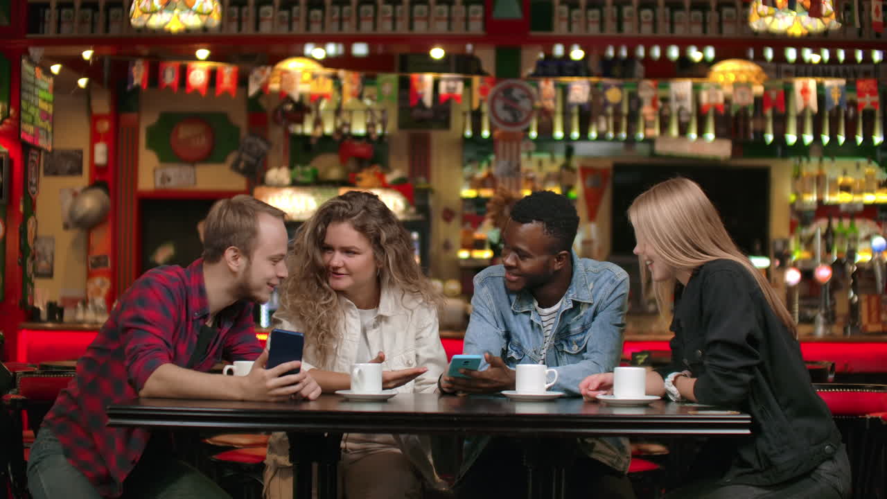 A multiethnic group of students three Europeans and an African American look at the phone screens laugh and discuss. Talk with friends and watch photos on the phone.