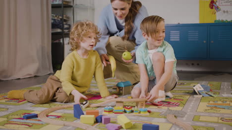Children-Playing-With-Cars-And-Pieces-Of-Wood-Sitting-On-A-Carpet-In-A-Montessori-School