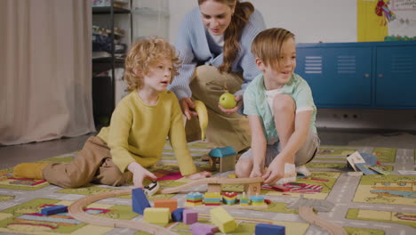 Kinder,-Die-Mit-Autos-Und-Holzstücken-Spielen,-Sitzen-Auf-Einem-Teppich-In-Einer-Montessori-Schule