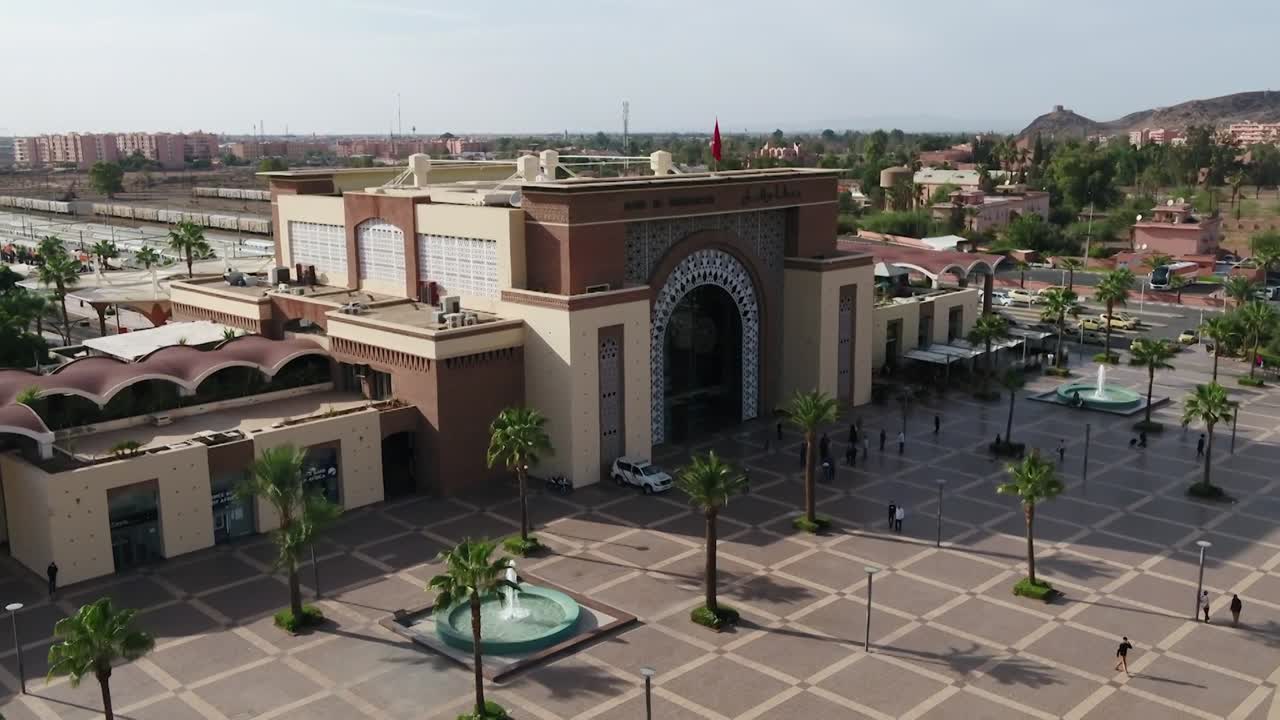 Marakeş Tren İstasyonu cephesinin detaylı drone çekimi. Büyük meydanı, çeşmeleri ve çevredeki şehri öne çıkararak İslami kemerlerin ve modern tasarımın çarpıcı birleşimini vurgular.