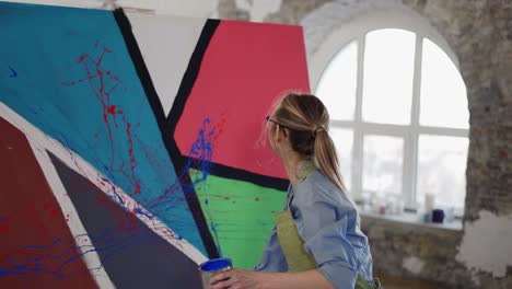 woman uses wide brush and color paints splashing gesture on canvas