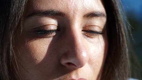 close up of sunshine illuminated female face, brown hair and eyes blink