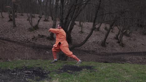 black belt kung fu master in orange uniform training in forest. wide shot