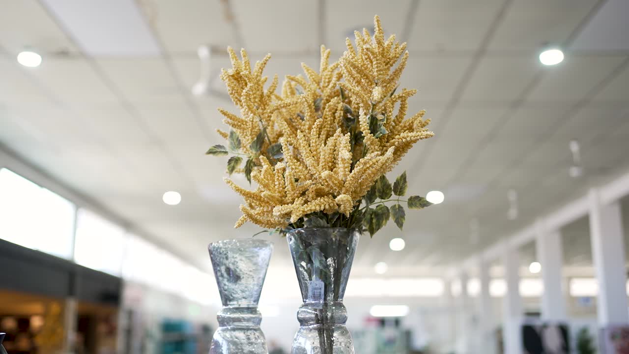 A bouquet of bright yellow flowers is placed in a clear vase. The setting is spacious, well-lit, and filled with soft colors, creating a warm atmosphere