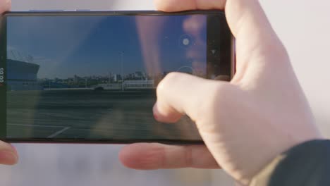 young woman records video via camera of professional racer drifting in circles on black car at track with mobile phone close screen view