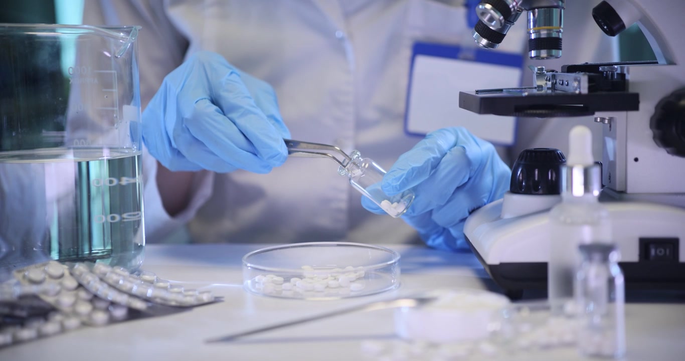 Pharmacist fills glass bottle with small pills at table in lab