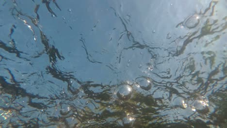 hermosas burbujas en la superficie del agua contra el cielo azul. vista submarina del rápido flujo de agua desde el fondo del río. patrón hipnótico abstracto. realismo surrealista. primer plano. 4k.