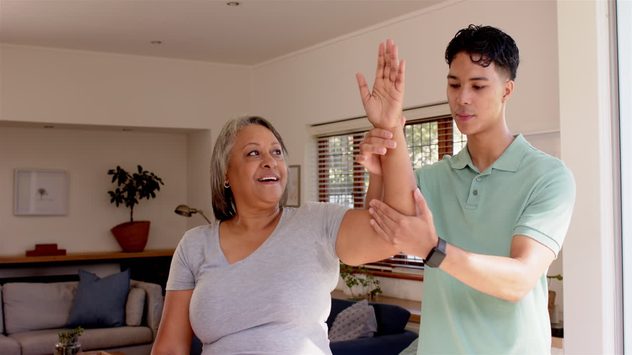 Physiotherapist assisting senior woman with arm exercises in living room