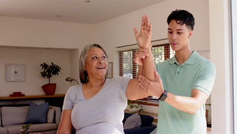 physiotherapist assisting senior woman with arm exercises in living room