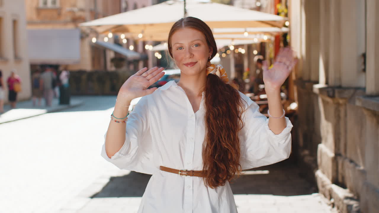 행복한 젊은 여성이 도시 거리에서 손을 흔들고 있습니다.