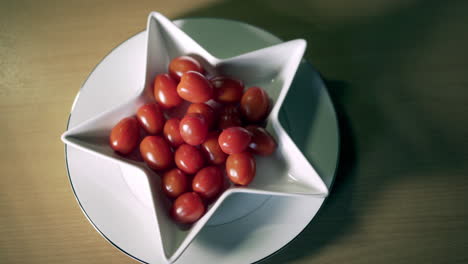 Tomates-De-Ciruela-Bebé-En-Un-Plato-En-Forma-De-Estrella-Con-La-Mano-Masculina-Tomando-Uno-Jugoso