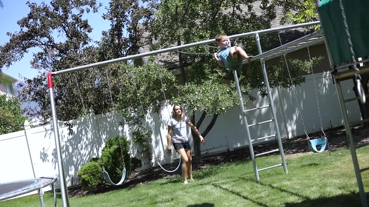 Slow Motion shot of a girl playfully pushing her younger brother on a swing on the playground in their backyard.