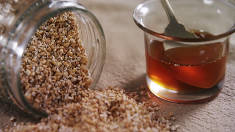 Grains-spilling-out-of-jar-with-bowl-of-honey-4k