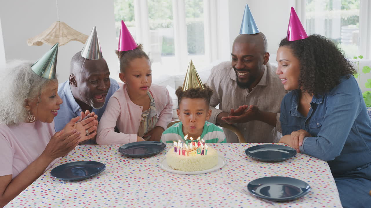 Multi Generation Family Sitting Around Table Celebrating At Boy's Birthday As He Blows Out Candles