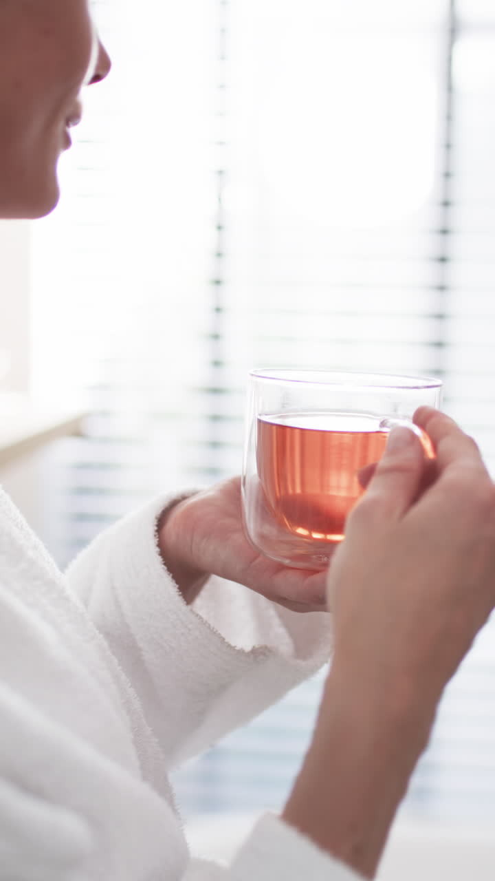 Vídeo vertical: Mulher caucasiana segurando caneca transparente com chá em casa