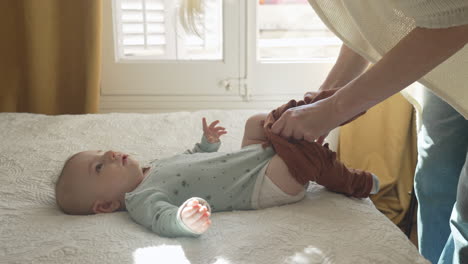 Mother-dressing-newborn-baby,-putting-pants-in-a-sun-lit-white-bedroom