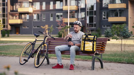 exhausted food delivery man seated on a bench having a cup of tea during his break