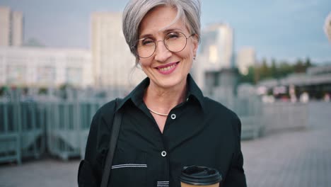 portrait senior business woman smiling confident independent female in city wearing black shirt. business lady drinking coffee during a break