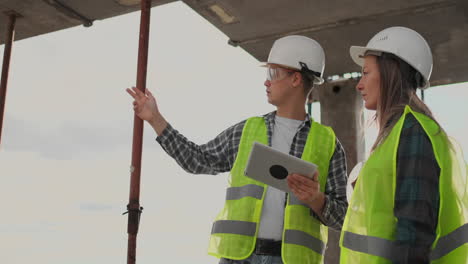 Un-Trabajador-De-La-Construcción-Y-Una-Arquitecta-Con-Casco-Discuten-El-Plan-De-Construcción-De-La-Casa-Y-Se-Cuentan-Sobre-El-Diseño-Sosteniendo-Una-Tableta,-Miran-El-Fondo-De-Los-Dibujos-De-Los-Rayos-Del-Sol.