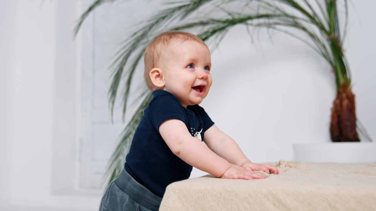 Hermoso bebé sonriendo adorablemente de pie en interiores. Niño pequeño intentando caminar. Fondo blanco.