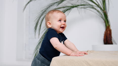 beautiful baby boy smiling adorably stands indoors. little child trying to walk. white backdrop.
