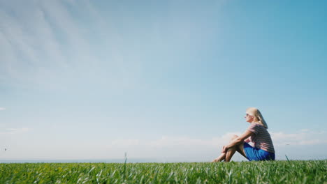 A-Woman-Is-Sitting-On-Perfect-Shorn-Grass-That-Goes-Into-A-Clear-Blue-Sky