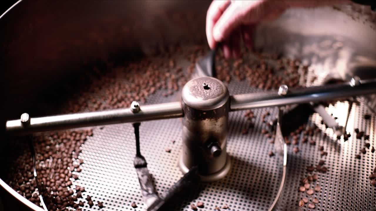 Man sweeping freshly roasted coffee beans from cooling bin as machine spins and turns