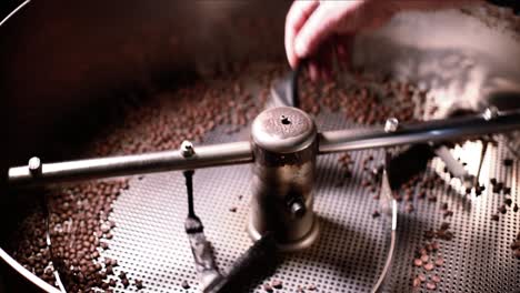 Mann-Fegt-Frisch-Geröstete-Kaffeebohnen-Aus-Dem-Kühlbehälter,-Während-Sich-Die-Maschine-Dreht-Und-Dreht