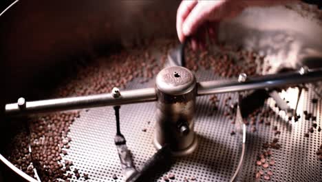 man sweeping freshly roasted coffee beans from cooling bin as machine spins and turns