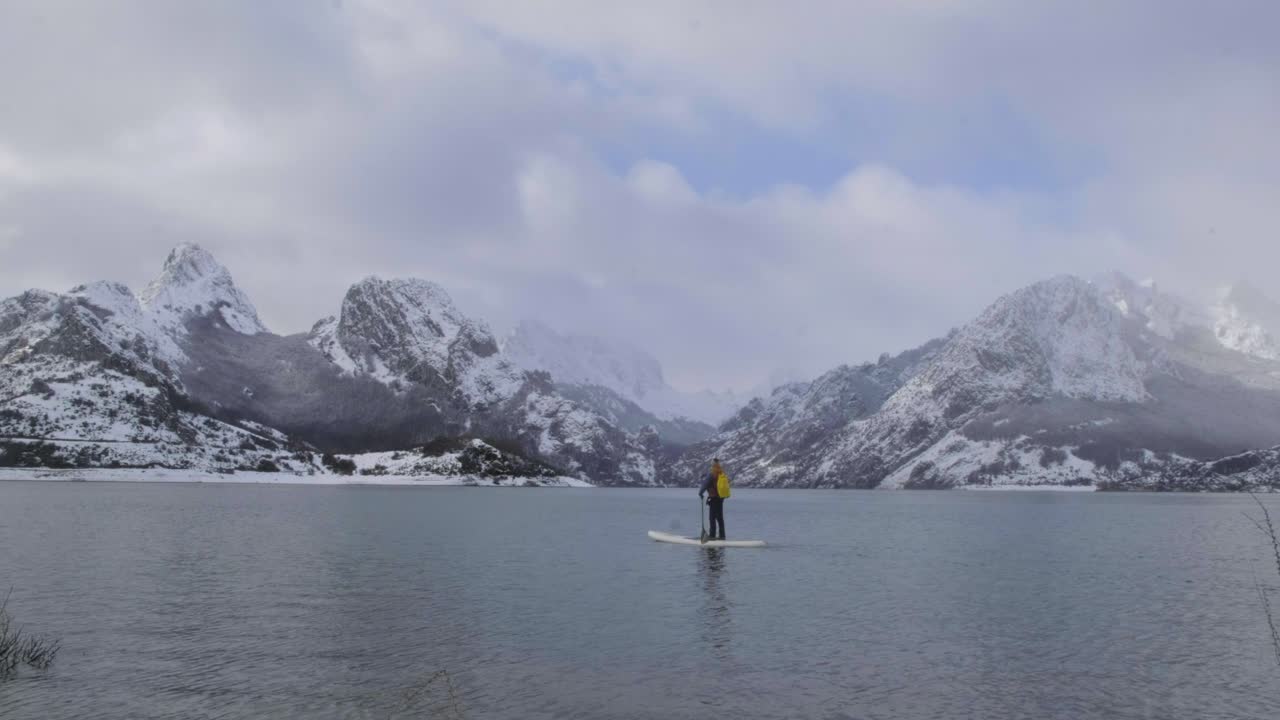 hombre en paddle board entre el agua y las montañas en la costa