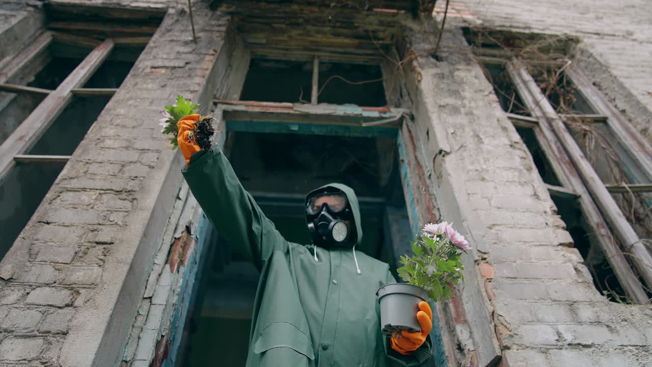 Ecological problems. Ecologist in protective gloves and suit pulling out fresh flowers from flower pot. Abandoned place. Biological attack.