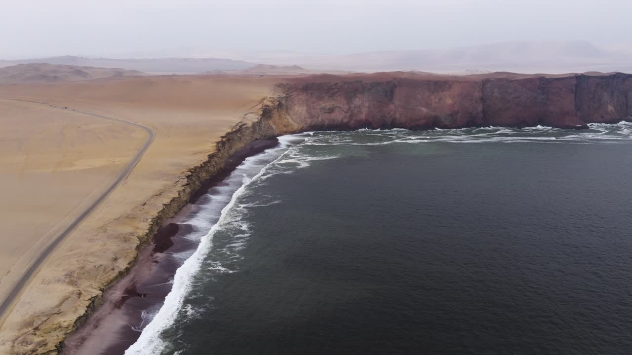 Steep cliffs dropping to dark surf where Paracas desert meets the Pacific, establishing pullback in slow motion