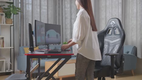 side view of asian female automotive designer walking into the studio sitting down and start working on 3d model of ev car on the desktop computers in the studio