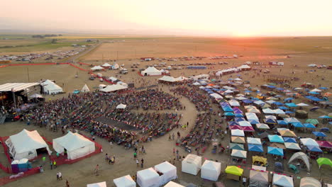 a drone circling an outdoor rock country music festival just before the sun goes down