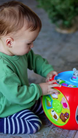peaceful one year old child playing with a toy on the floor. baby boy turns the toy and presses buttons on it. vertical video