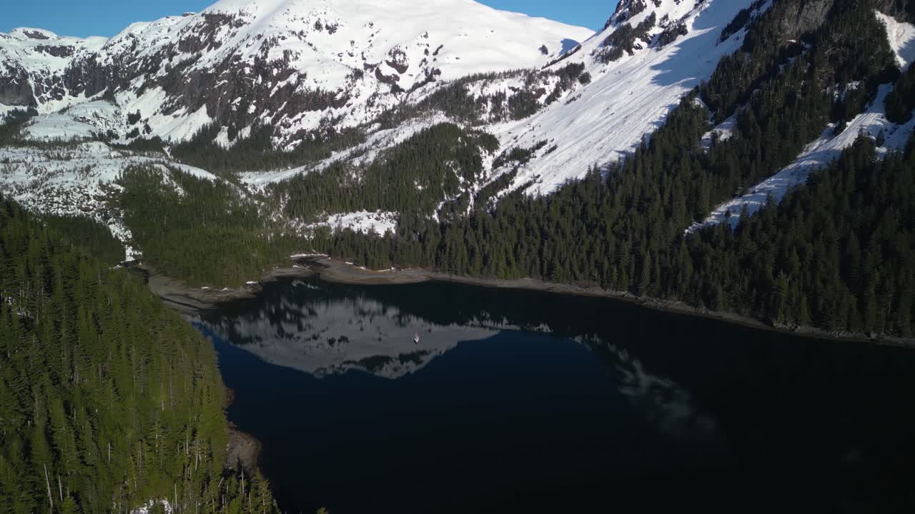 tomada panorámica de un avión no tripulado rodeando un velero anclado en medio de las montañas nevadas de la soleada alaska