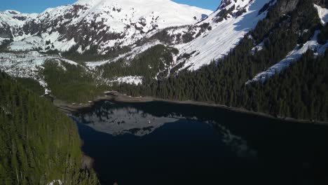 Panoramic-drone-shot-circling-a-sailboat-anchored-in-middle-of-snowy-mountains-of-sunny-Alaska