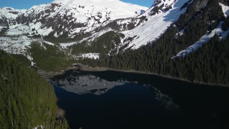 panoramic drone shot circling a sailboat anchored in middle of snowy mountains of sunny alaska